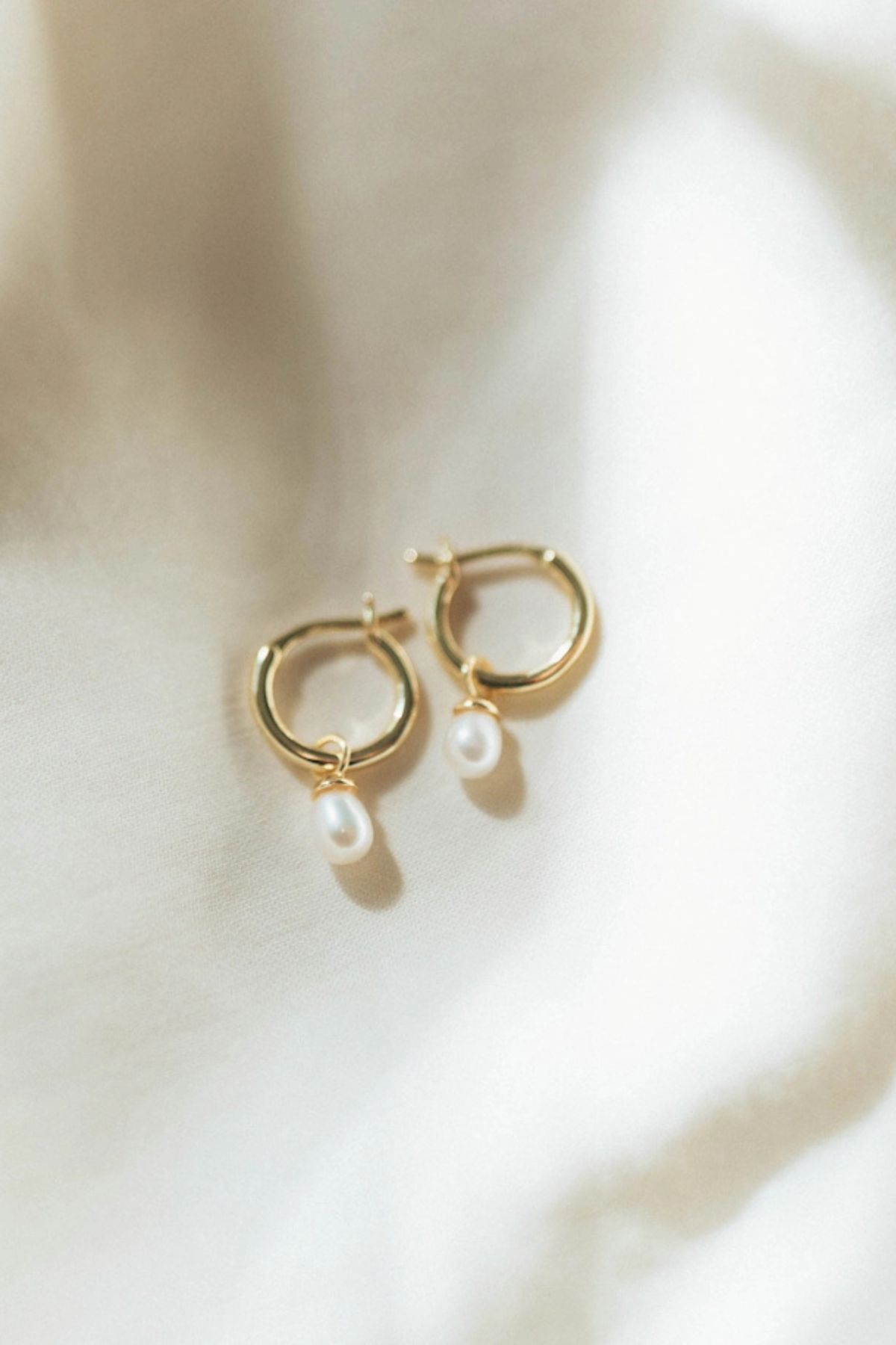 Gold hoop earrings with pearls on a light background