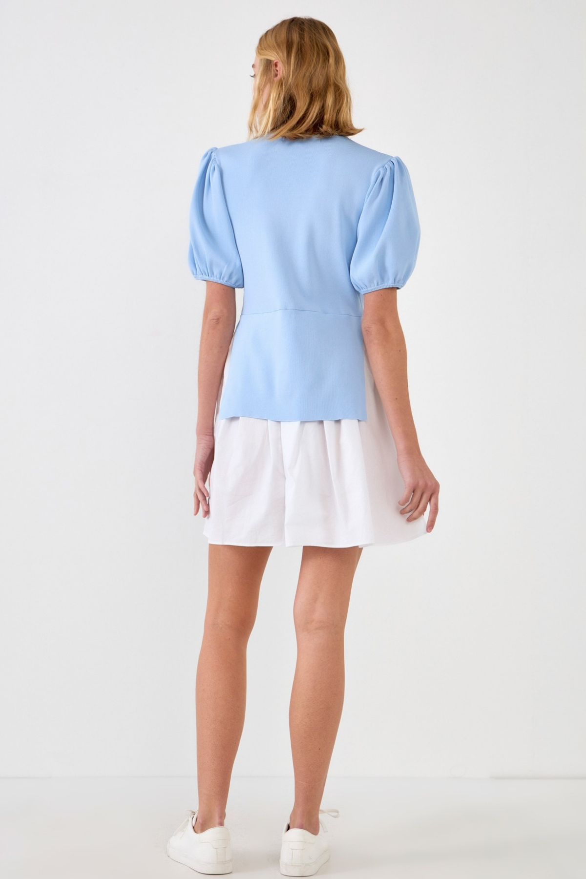Woman wearing a light blue blouse dress and white skirt on a white background