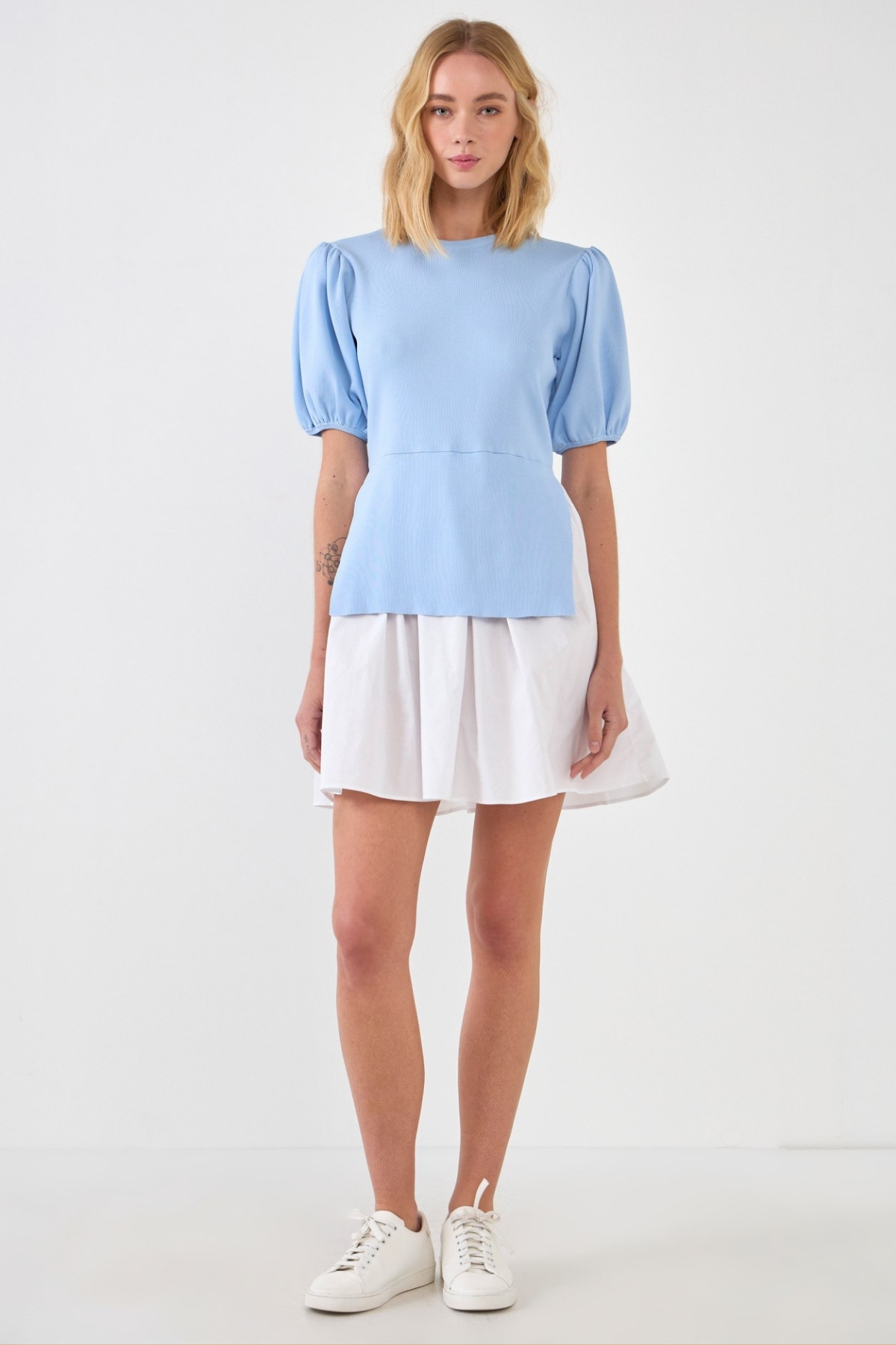 Woman wearing a light blue blouse dress and white skirt on a white background