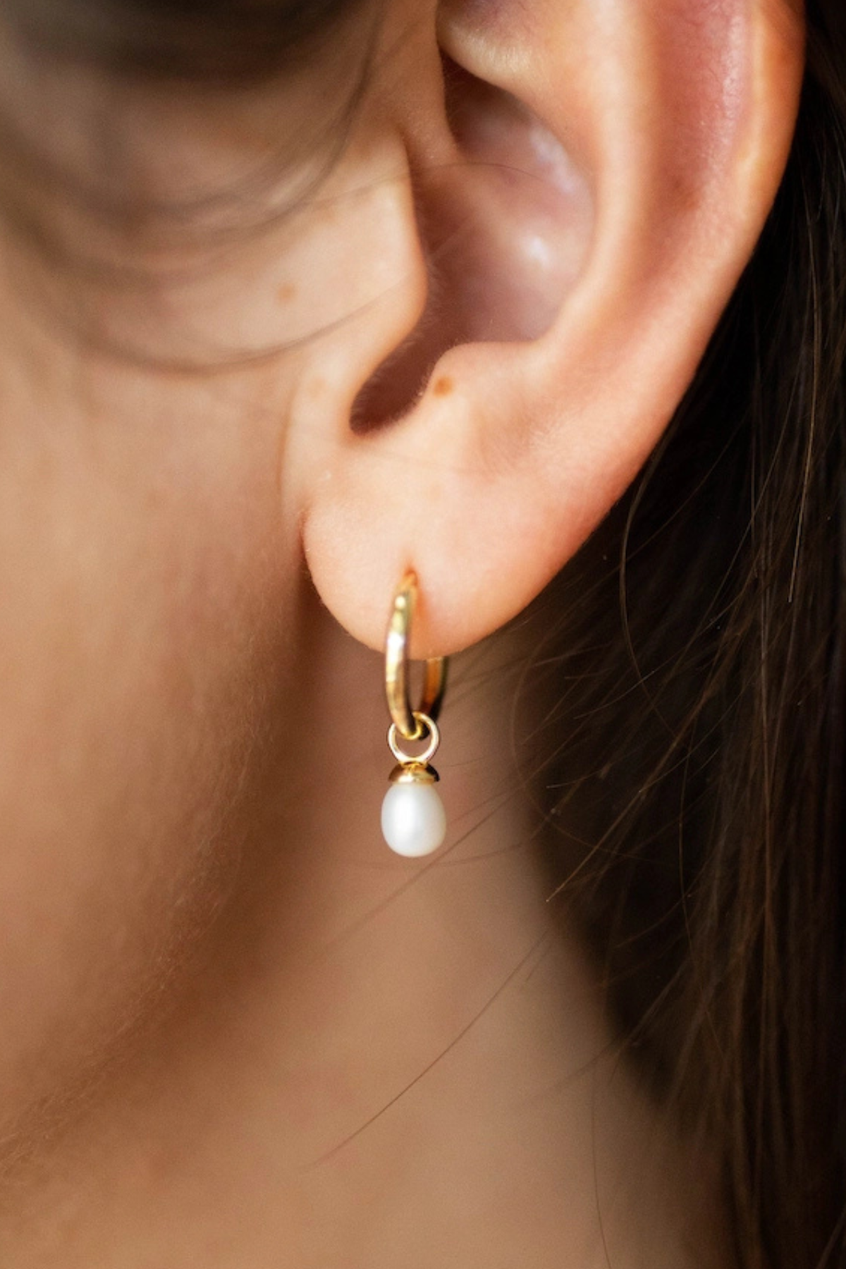 Close-up of an ear wearing a gold hoop earring with a pearl drop.