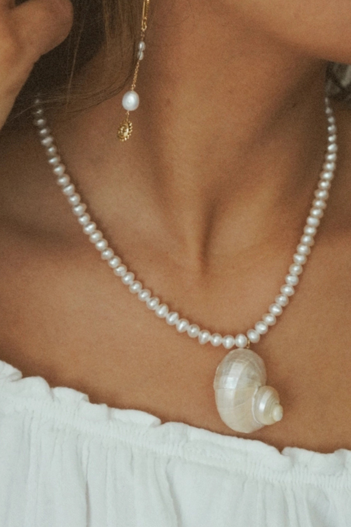 Pearl necklace with a shell pendant worn by a person against a white background