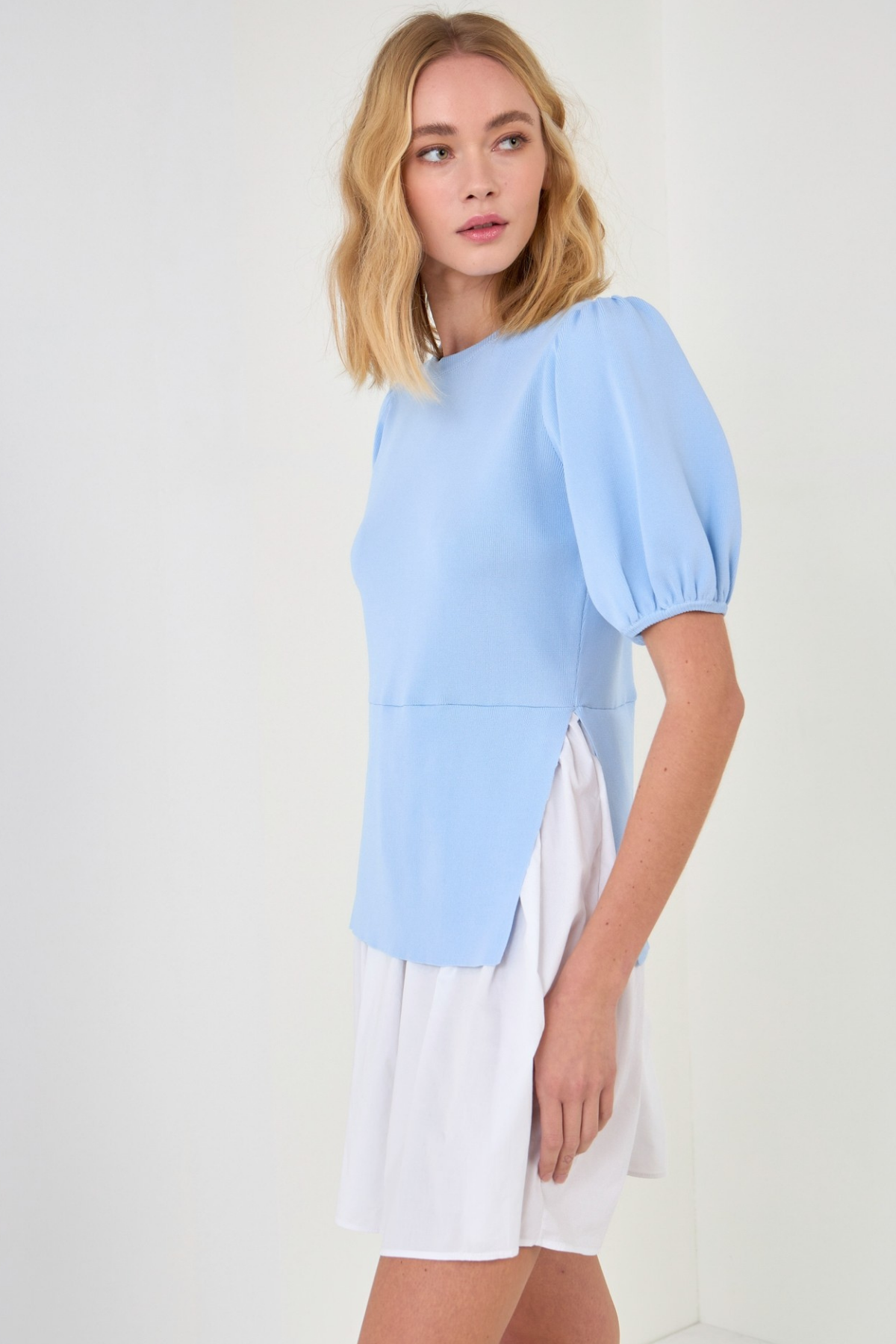 Woman wearing a light blue blouse dress and white skirt on a white background